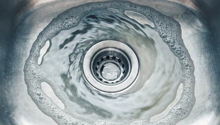 Foaming water swirling down a steel sink drain