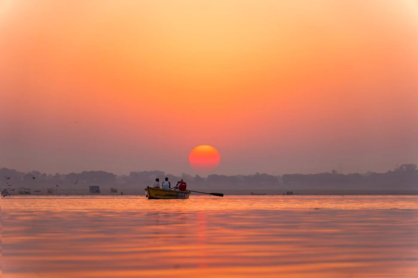 A small boat on open water heading toward the sun