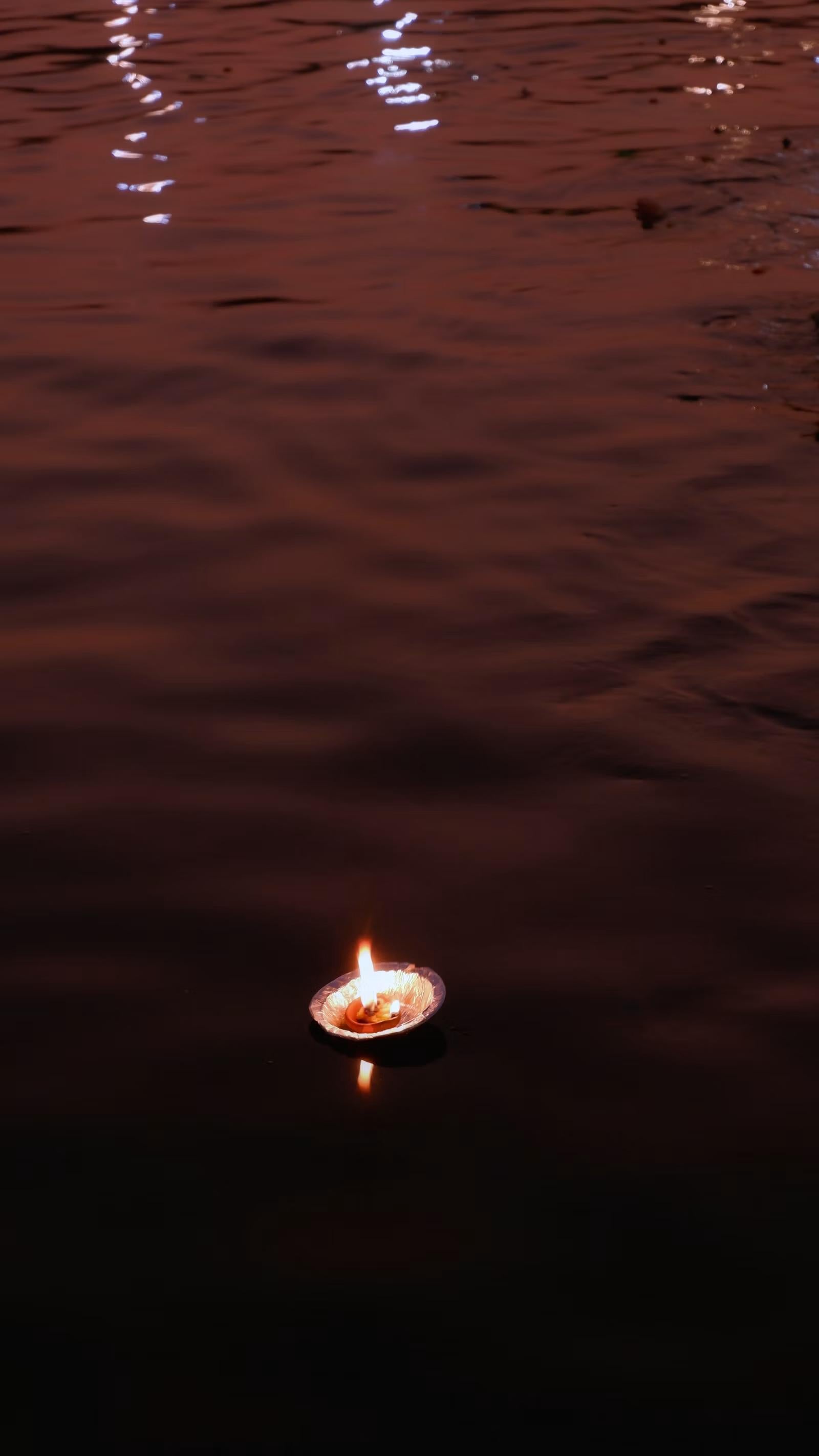 A single lit diya floating alone on dark river water
